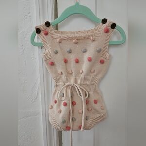 Beige knitted baby romper with pom poms